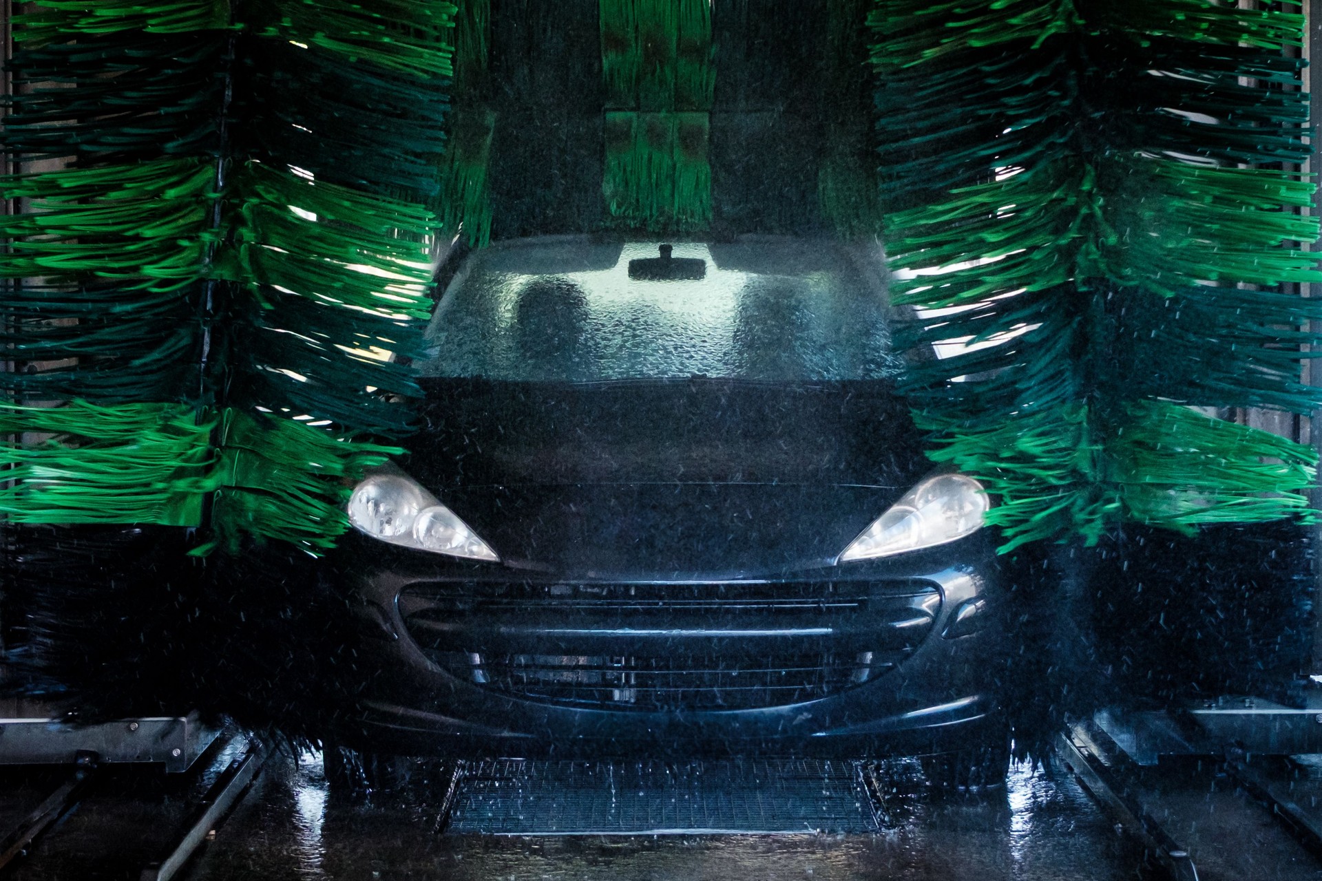 Automatic car wash cleaning black car with green brushes